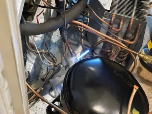 Technician brazing new copper connections on a Sub-Zero compressor during a full sealed system rebuild